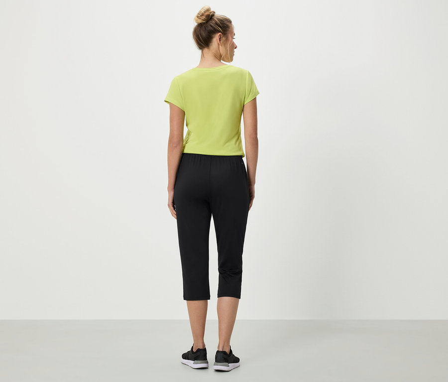 Frau von hinten in hellgrünem T-Shirt, schwarzen Caprihosen und Turnschuhen.