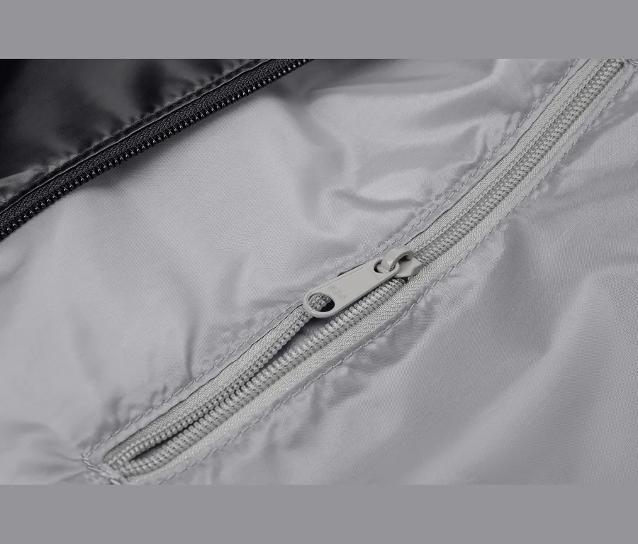 Nahaufnahme eines grauen Stoffes mit einem teilweise geöffneten grauen Reißverschluss. Oben links ist ein schwarzer Stoff mit einem schwarzen Reißverschluss zu sehen.