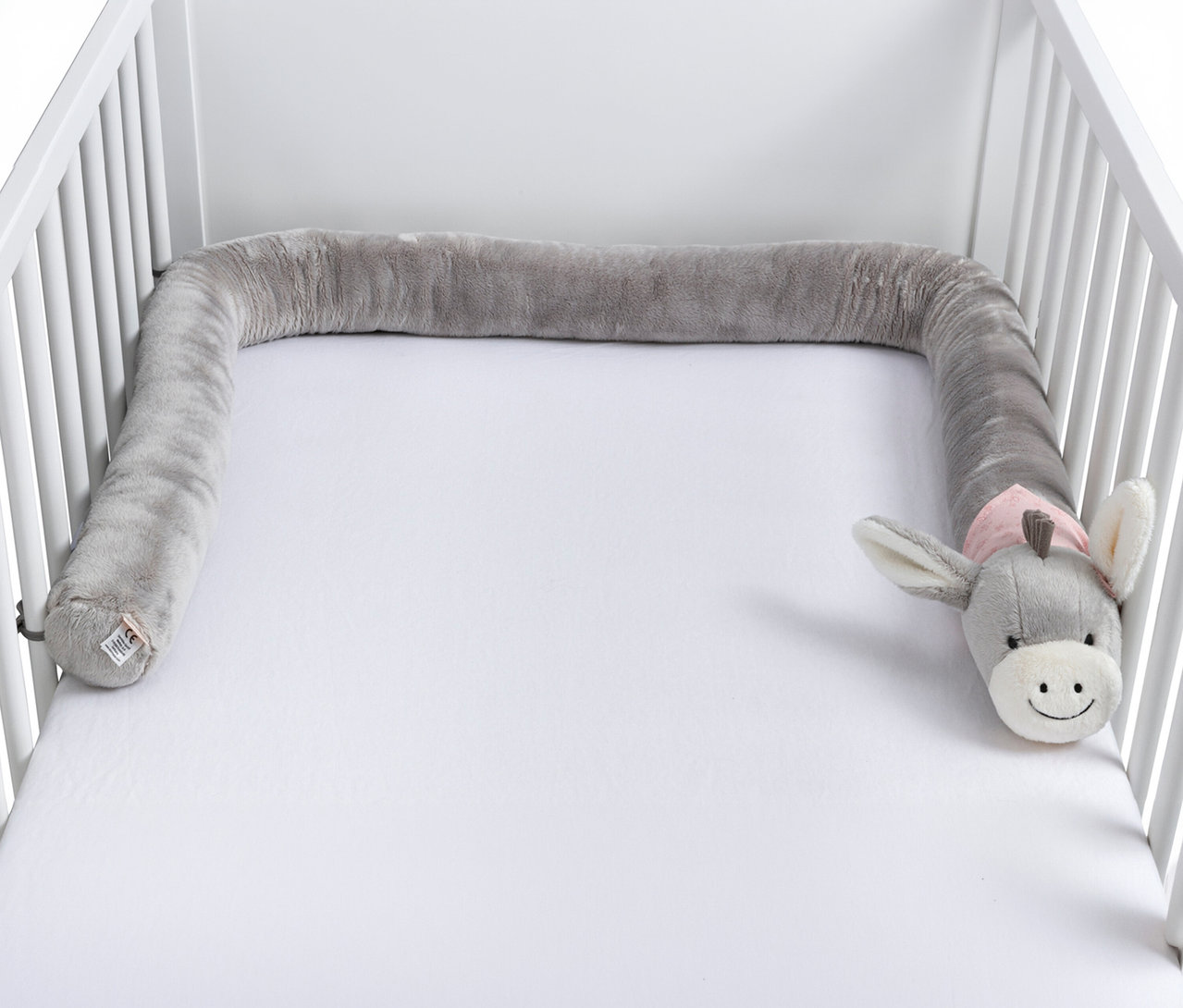 Graue, plüschige Bettschlange mit einem Eselkopf, die in einem weißen Babybett liegt.