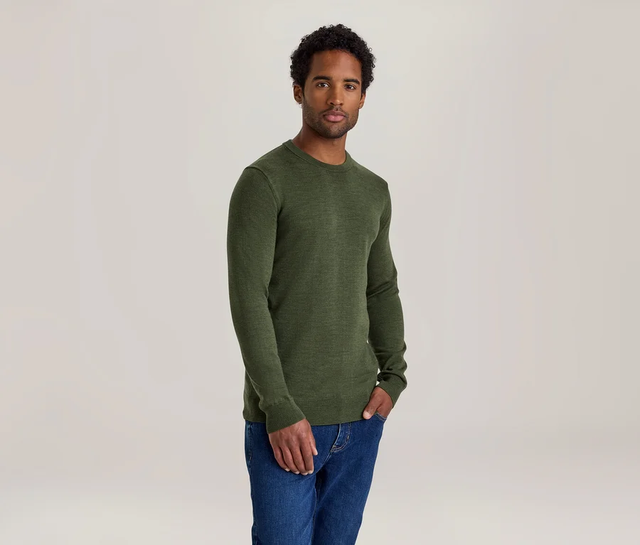 Mann mit dunklen Locken trägt ein grünes Langarmshirt und blaue Jeans, eine Hand in der Hosentasche.