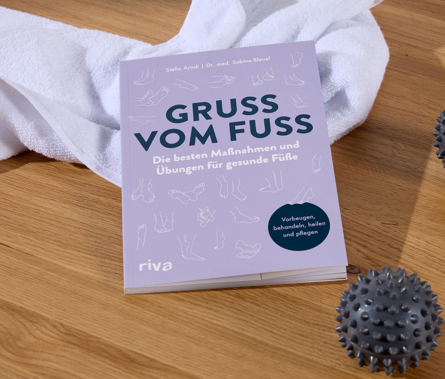 Das Buch Gruss Vom Fuss neben einem weißen Handtuch und zwei Massagebällen auf einem Holzboden.