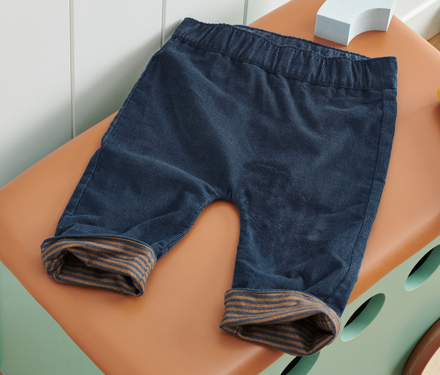 Eine blaue Wende-Schlupfhose liegt auf einer braunen Spielzeugkiste.