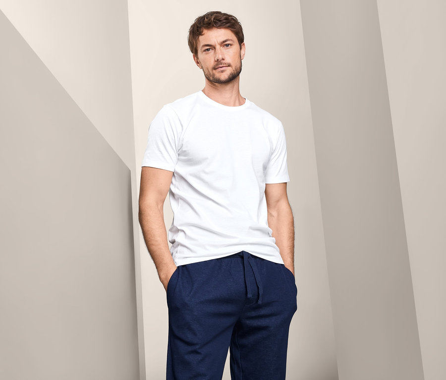 Mann posiert vor einem Hintergrund und trägt ein weißes 2 T-Shirts mit Rundhals-Ausschnitt.