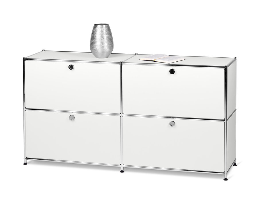 Ein weißes Sideboard Metall »CN3« mit 4 Klappfächern. Oben auf dem Schrank stehen eine silberne Vase und ein offenes Buch.