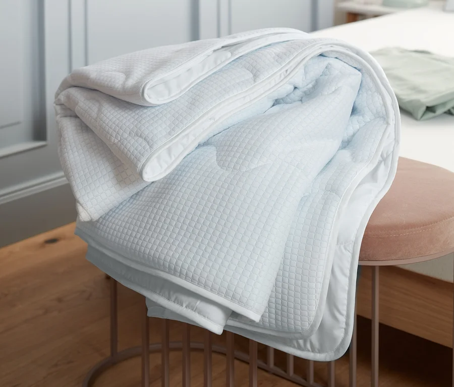 Eine gefaltete kühlende Bettdecke liegt auf einem rosafarbenen Hocker in einem Schlafzimmer.