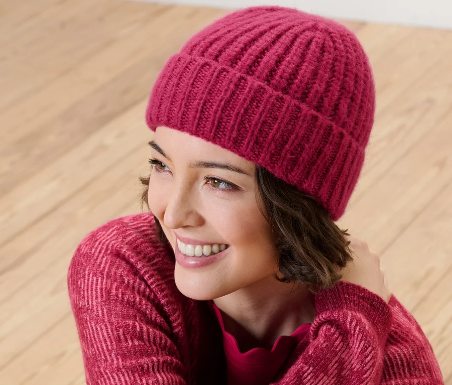 Lächelnde Frau trägt eine himbeerfarbene Strickmütze.