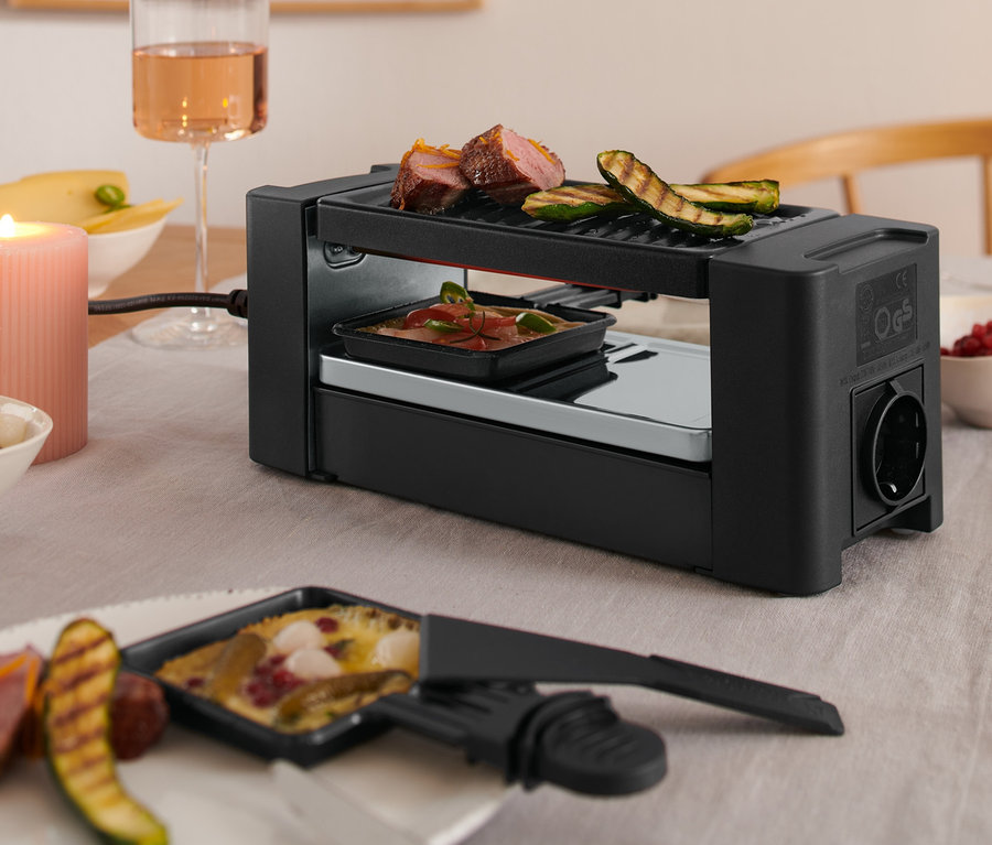 Detailaufnahme eines Tisches mit einem Raclette für Zwei, einem Glas Wein und Speisen.