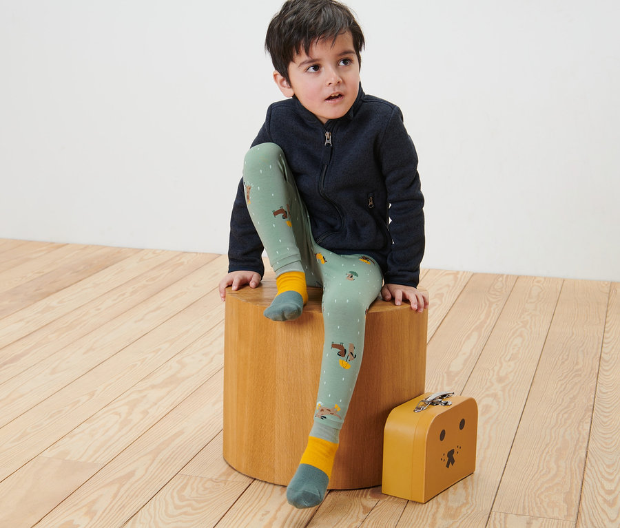 Junge sitzt auf einem Holzhocker und trägt 2 Kinder-Leggings.