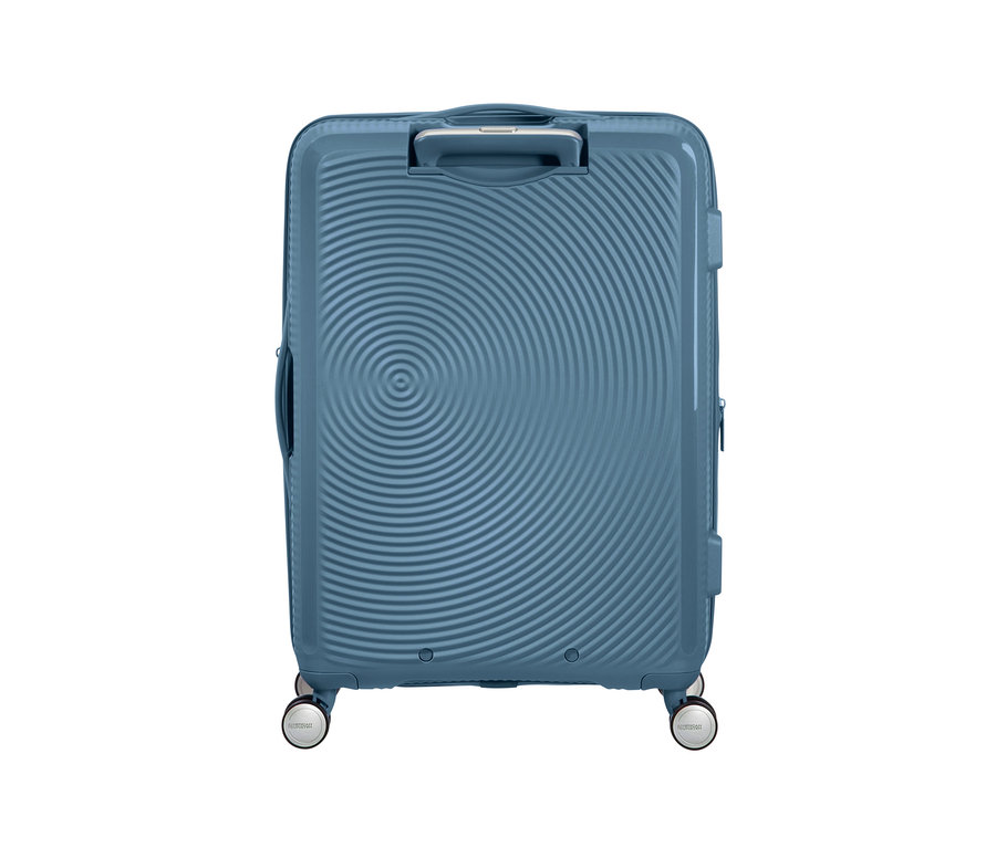 Ein mittelgroßer, stone blue American Tourister Hartschalen-Koffer »Soundbox« Spinner vor weißem Hintergrund.