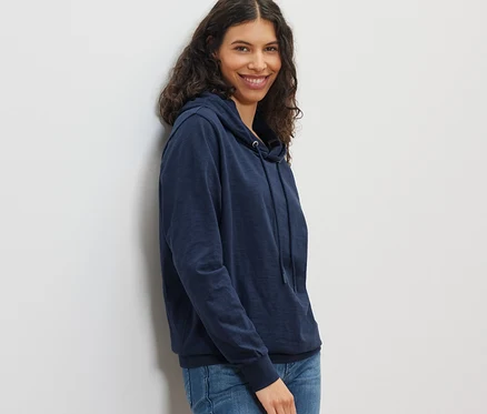 Lächelnde Frau posiert in marineblauem Jersey-Hoodie und Jeans.