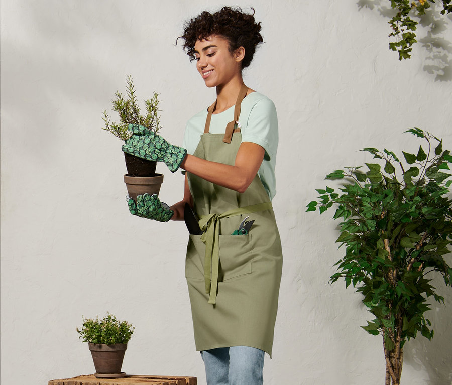 Frau mit Gartenschürze hält Blumentopf.