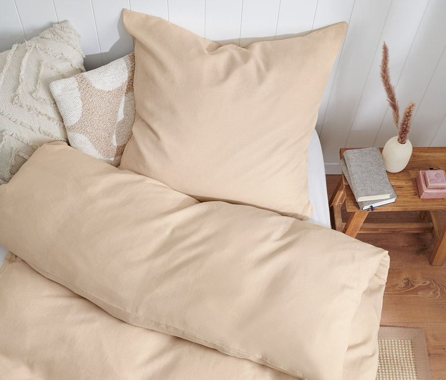 Beige Bettwäsche aus gewaschenem Leinen in Normalgröße, Doppelgröße und Übergröße auf einem Bett mit weißem Kopfteil.
