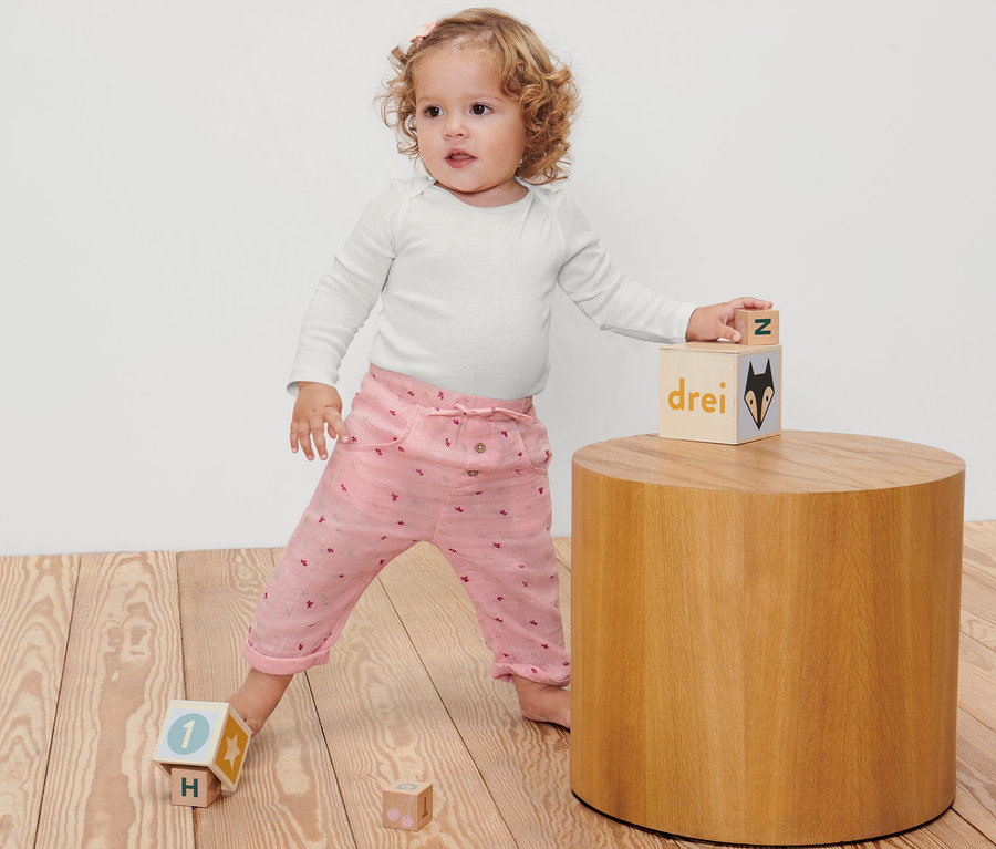 Ein Kleinkind spielt mit Bauklötzen auf einem Holzboden und trägt eine Baby-Schlupfhose.