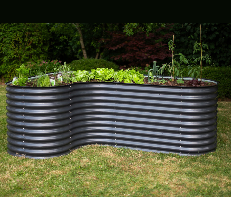 Ein schwarzes Hochbeet in L-Form steht auf einem Rasen.