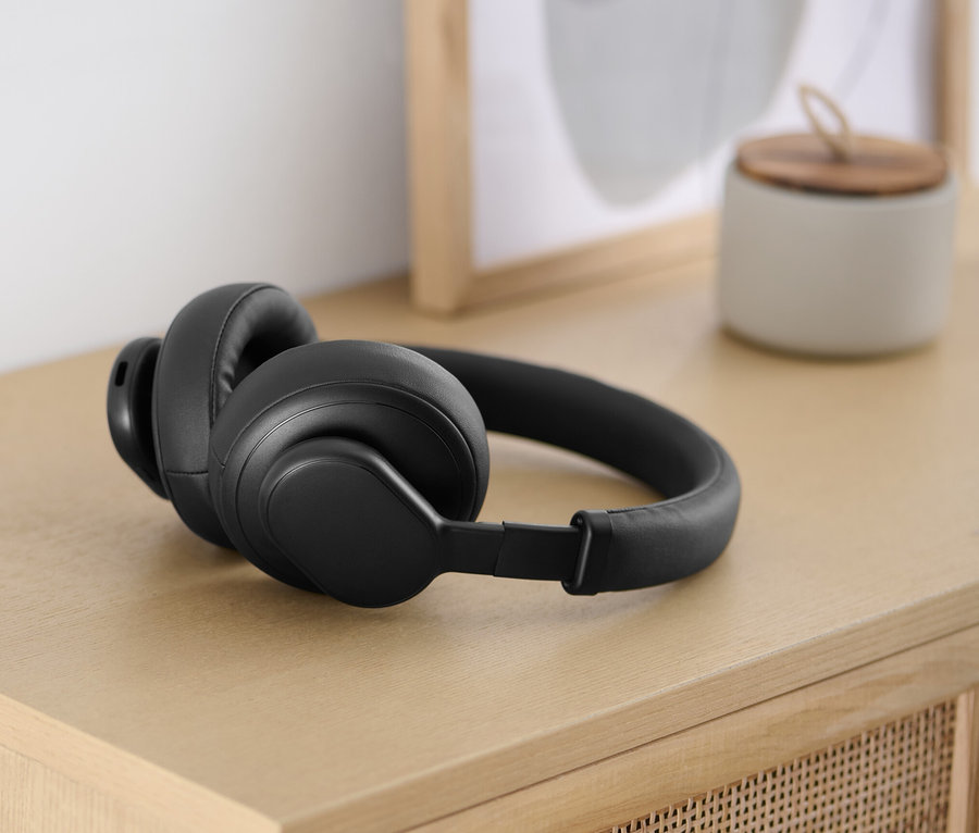 Schwarze Bluetooth®-Kopfhörer mit Touchfunktion liegen auf einem hellen Holztisch.