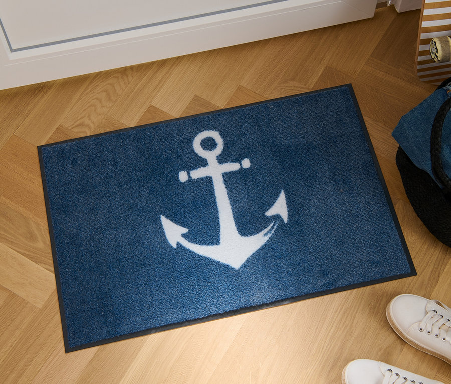 Eine Textil-Fußmatte mit Ankermotiv liegt auf einem Parkettboden.