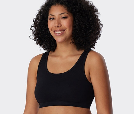 Frau mit lockigem Haar trägt ein schwarzes 2 SCHIESSER Bustiers mit Bio-Baumwolle.