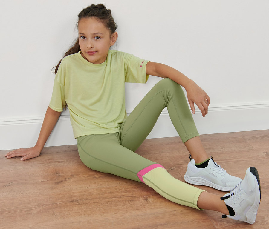 Mädchen sitzt am Boden und trägt eine grüne Kinder-Sporttight.