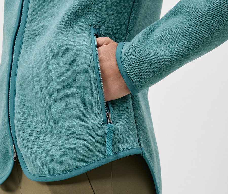 Detailaufnahme einer türkisfarbenen Fleecejacke mit einer Hand in der Tasche.