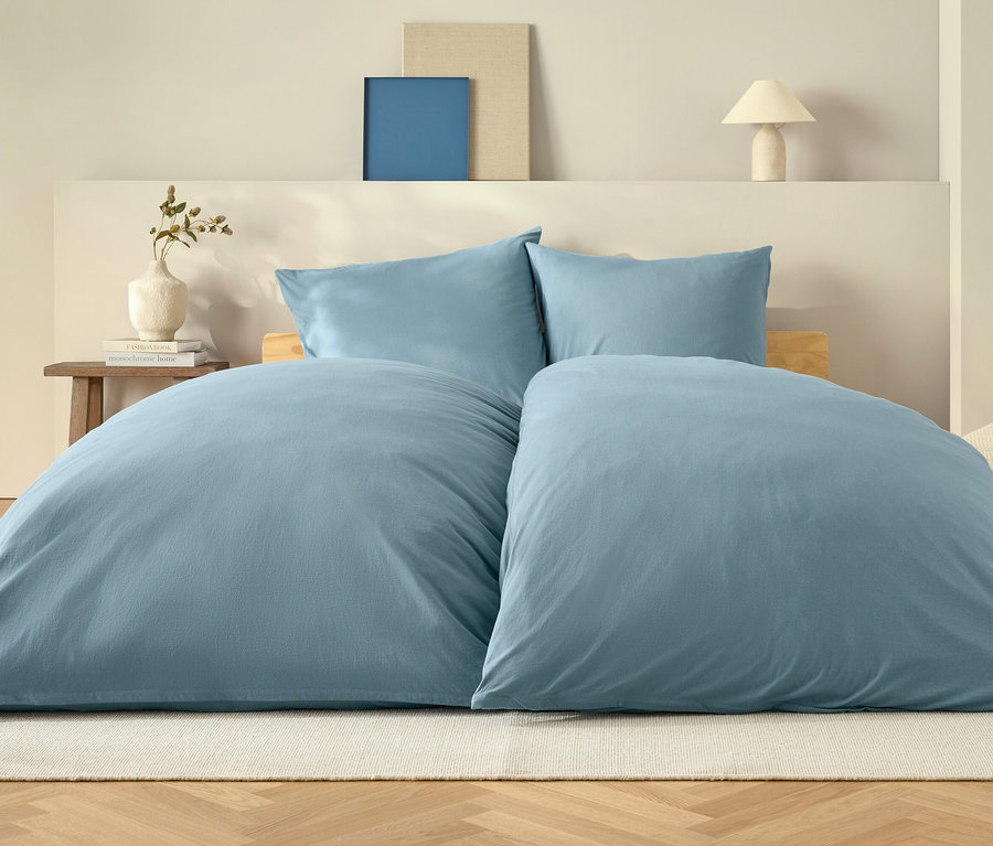 Blaue Bettdecke und zwei Kissen auf einem Bett auf einem weißen Teppich.