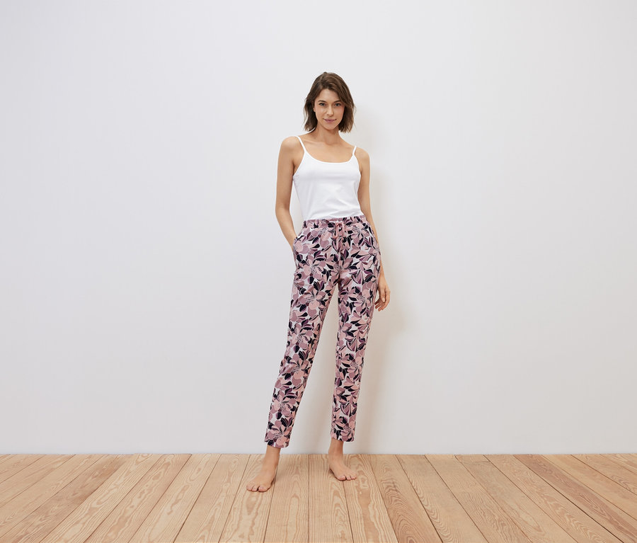 Frau steht mit Händen in den Taschen einer geblümten Hose, weißes Top.