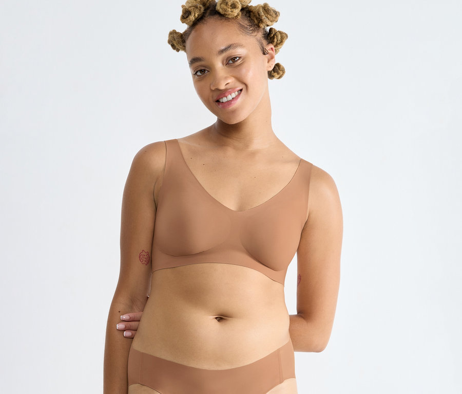 Lachende Frau mit Duttfrisur trägt einen sloggi ZERO Feel 2.0 Bralette in Nostalgic Brown und passende Unterwäsche.