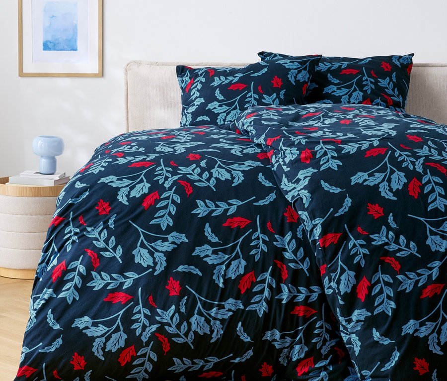 Bett mit dunkelblauer Bettwäsche mit roten und blauen Blättern.