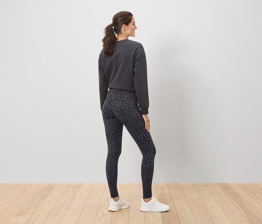 Frau posiert in grauem Pullover und Leggings mit Leopardenmuster.