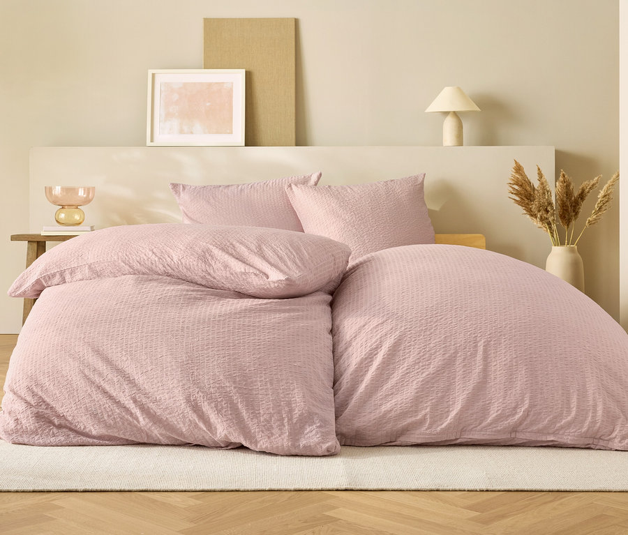 Rosa Bettwäsche auf einem Bett vor beigem Hintergrund.