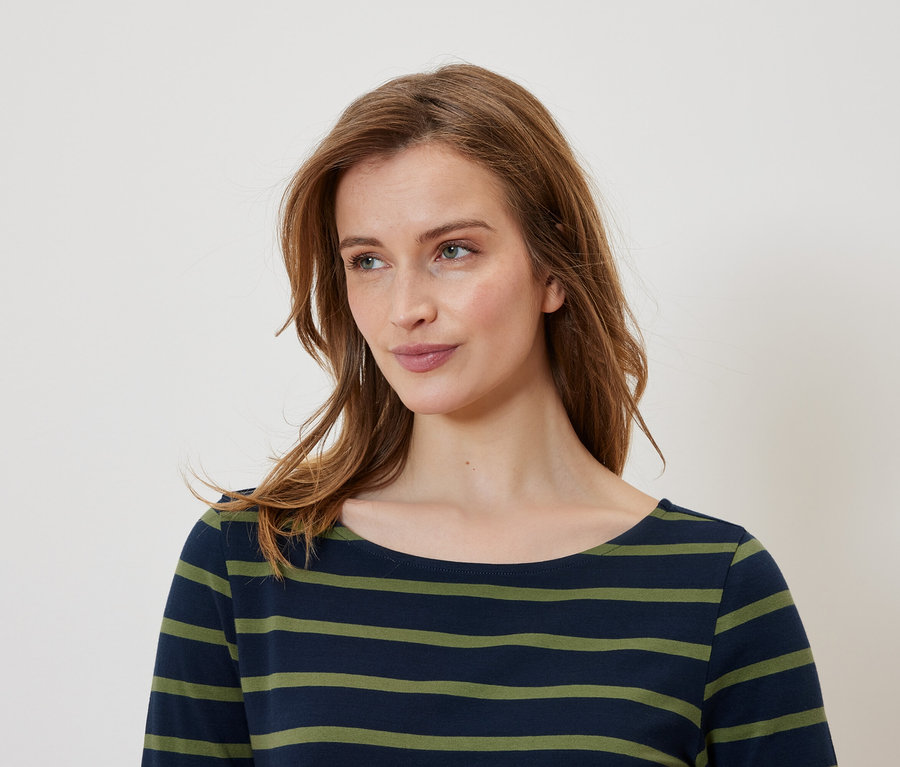 Porträt einer Frau mit braunen Haaren, die ein blau-grün gestreiftes T-Shirt trägt.