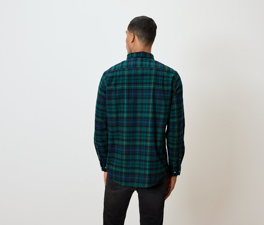 Ein Mann mit dem Rücken zur Kamera trägt ein grünes kariertes Hemd und schwarze Jeans.