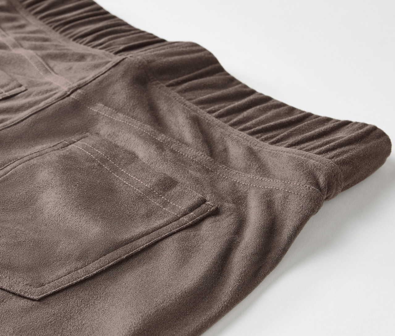 Detailaufnahme einer braunen Wildlederhose mit elastischem Bund und Gesäßtasche.