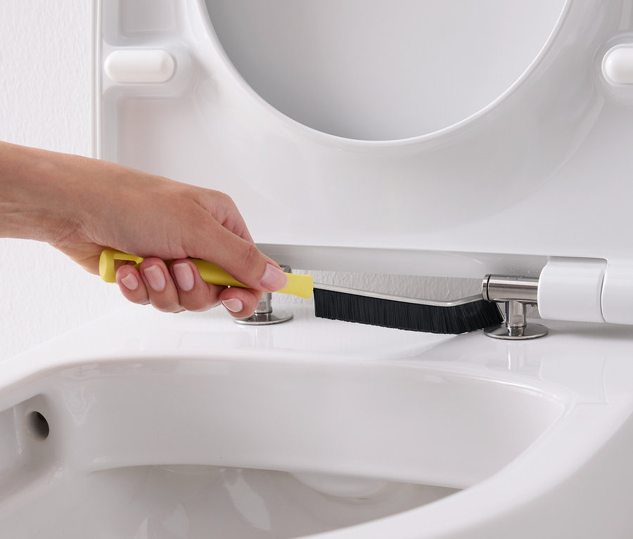 Eine Hand reinigt mit einer gelben Bürste einen weißen Toilettensitz.