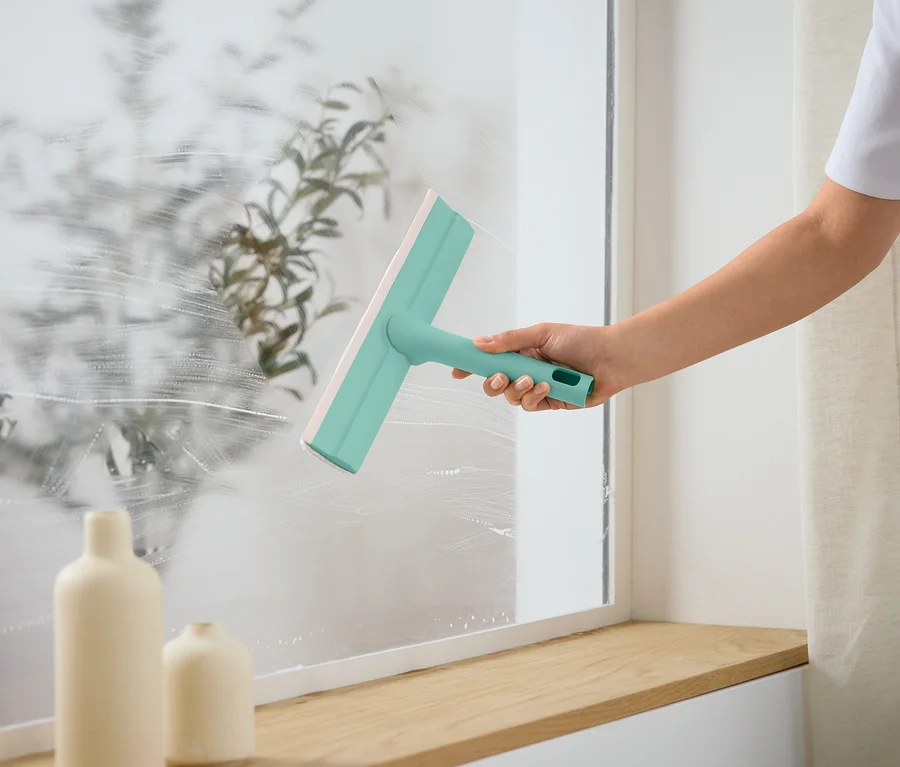 Person putzt Fenster mit einem Fensterabzieher.