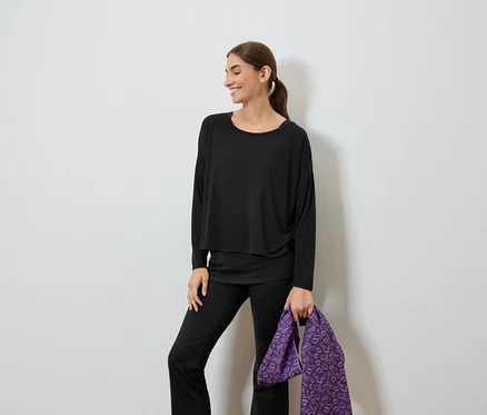 Lächelnde Frau in schwarzer Kleidung hält eine violette Tasche.