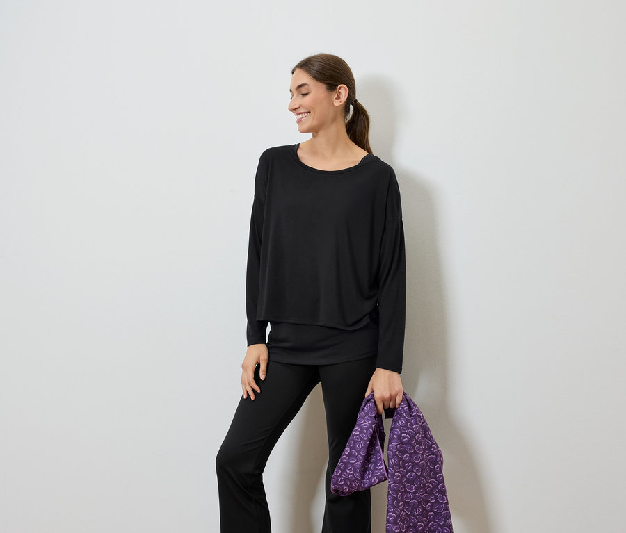 Lächelnde Frau in schwarzer Kleidung hält eine violette Tasche.