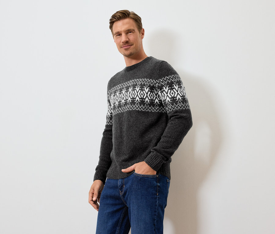 Mann posiert in grauem Pullover mit Muster und blauen Jeans.