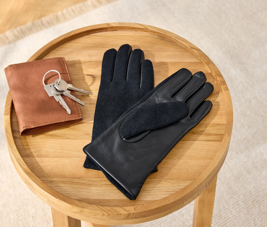 Auf einem Holzhocker liegen eine braune Ledergeldbörse mit Schlüsseln und ein Paar schwarze Lederhandschuhe.