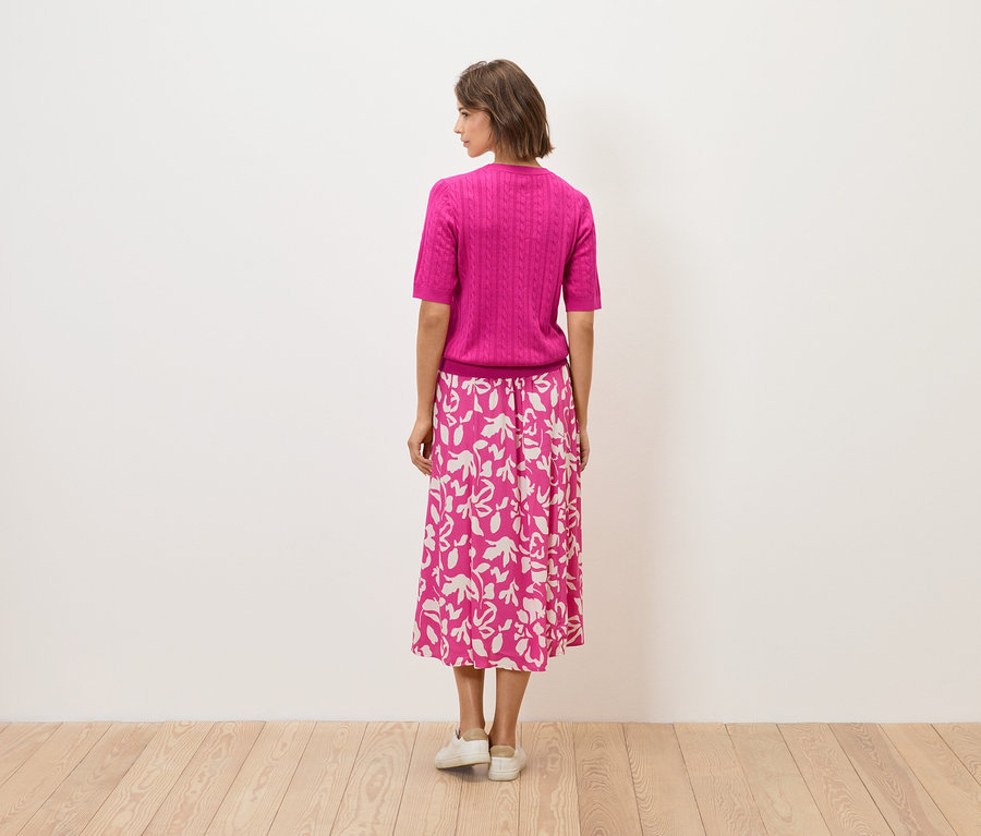 Eine Frau steht mit dem Rücken zur Kamera, sie trägt ein pinkes Oberteil und einen Rock mit Blumenmuster.