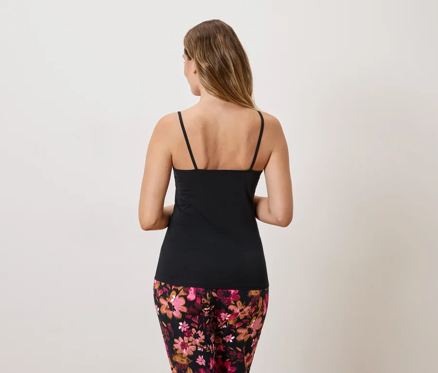 Rückansicht einer Frau mit langem, blondem Haar, die ein schwarzes Tanktop und eine blumengemusterte Hose trägt.