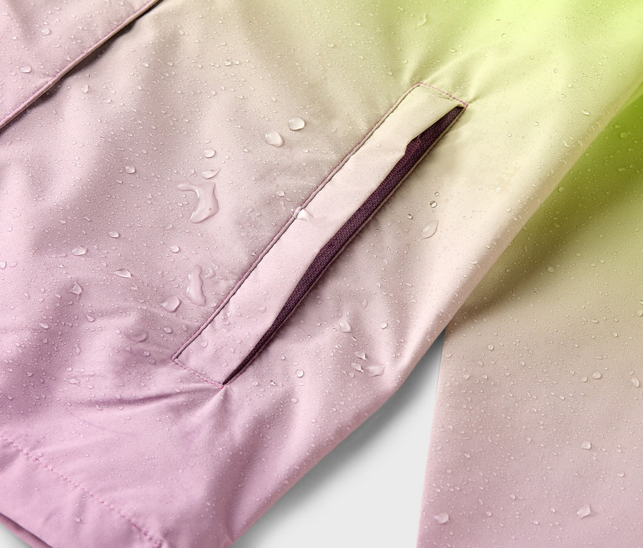 Detailaufnahme einer wasserabweisenden Jacke in einem Farbverlauf von Rosa nach Gelb mit Regentropfen und einer Seitentasche.