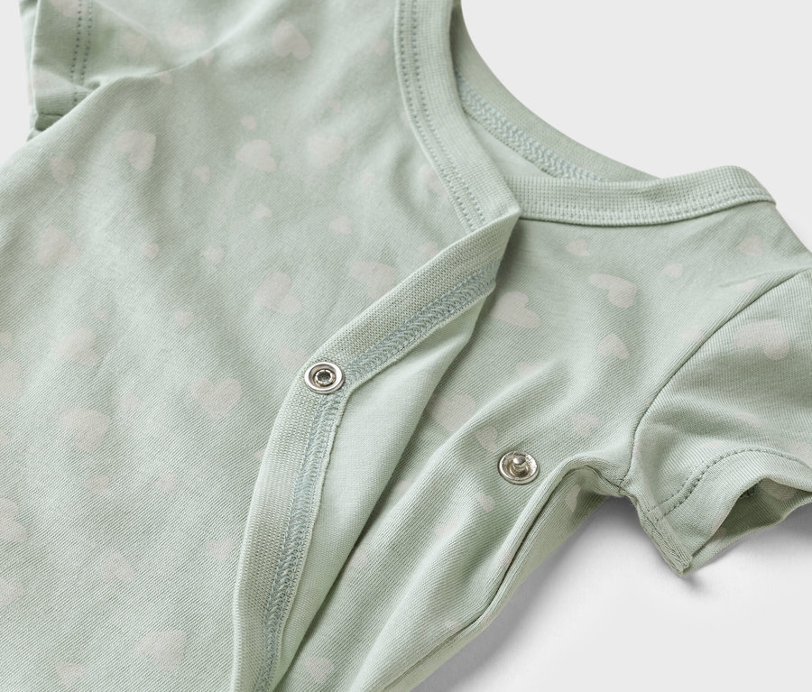 Detailaufnahme eines hellgrünen Babybodys mit weißem Herzchenmuster und Druckknöpfen.