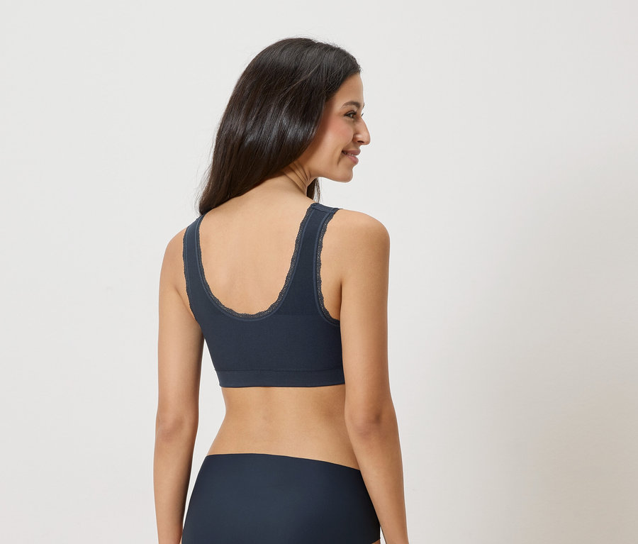 Frau trägt marineblauen BH mit Spitzenbesatz und passende Unterwäsche, von hinten gesehen.