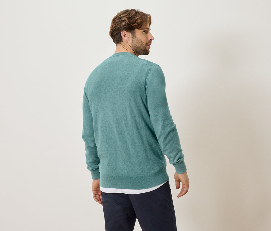 Mann von hinten in türkisfarbenem Pullover und blauer Hose.