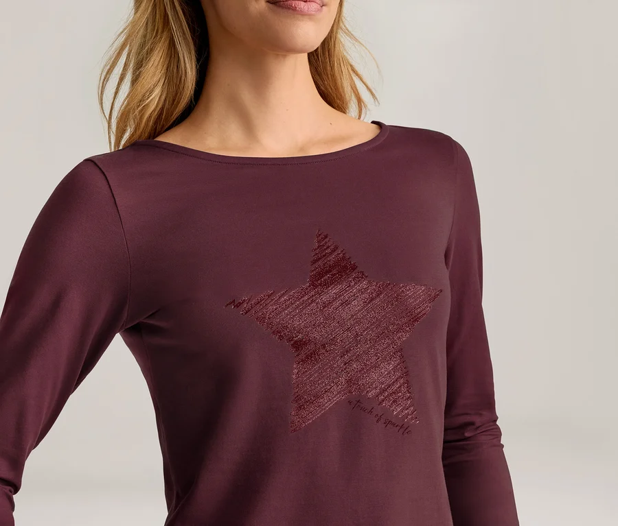 Frau trägt ein dunkelrotes Langarmshirt mit U-Boot-Ausschnitt und einem großen, strukturierten, gekritzelten Sternmotiv auf der Vorderseite.