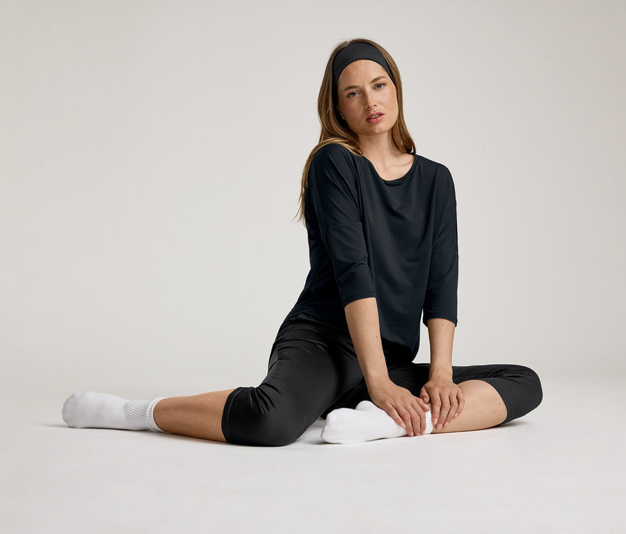 Frau sitzt mit schwarzem 3/4-Sportshirt. Sie trägt ein Stirnband und weiße Socken.