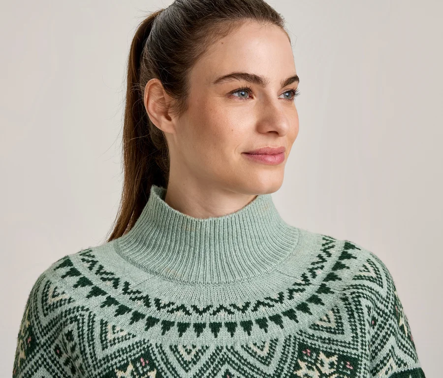 Frau blickt nach rechts, trägt einen hellgrünen Rollkragenpullover mit dunkelgrünem, cremefarbenem und rosa Muster.