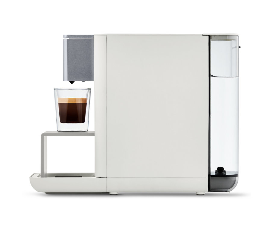 Qbo ESSENTIAL Bright Sand Kaffeemaschine mit einer Tasse Kaffee.