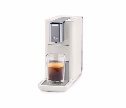 Qbo ESSENTIAL Bright Sand Kaffeemaschine mit Tasse Kaffee.