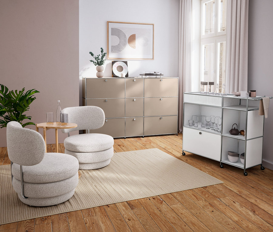 Modernes Wohnzimmer mit zwei hellgrauen Sesseln, einem runden Anstelltisch aus Massivholz, beigem Sideboard und weißem Servierwagen.